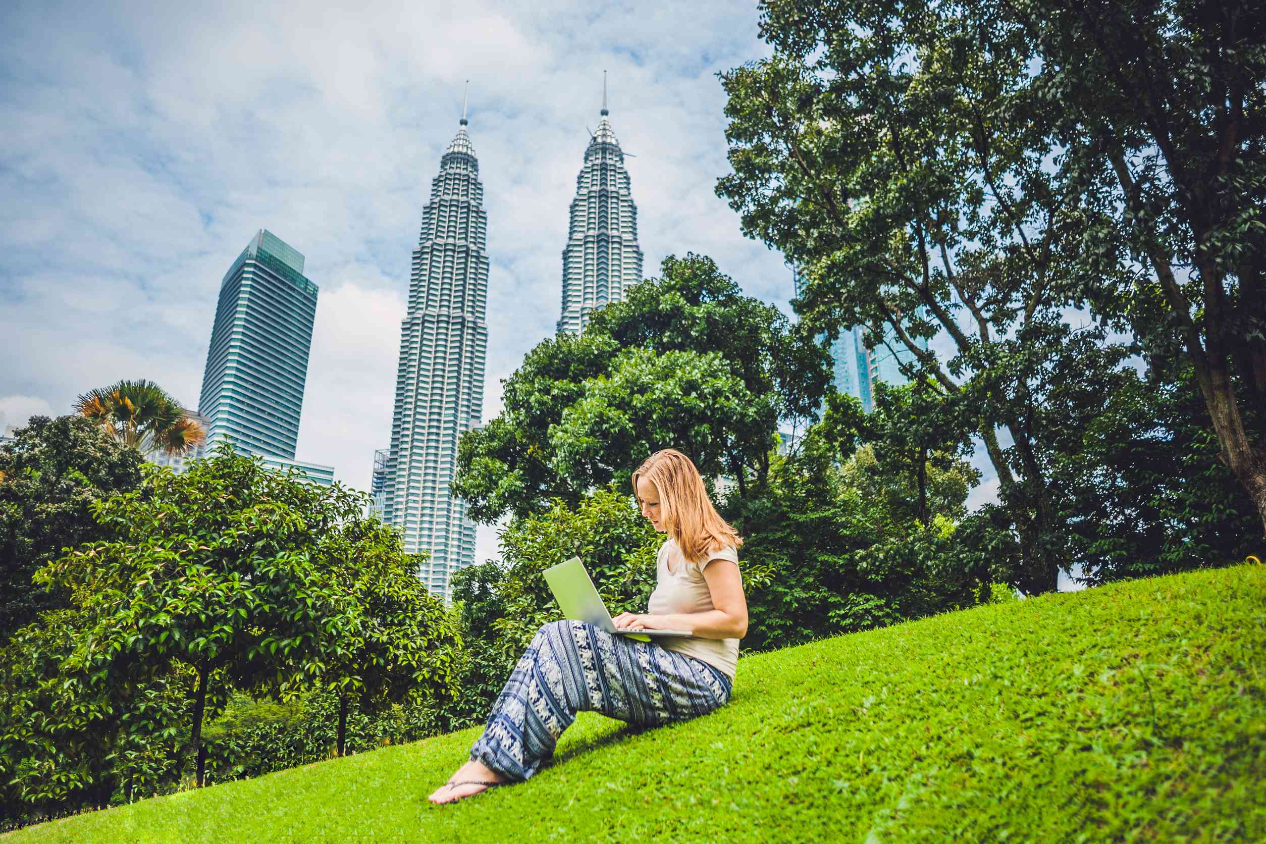 Young Woman In Casual Dress Using Laptop In A Tropical Park On The Background
